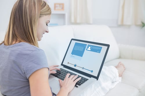Woman sitting on sofa and checking her social media profile on the laptop